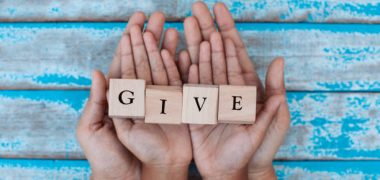 Alphabet letter wooden blocks with words GIVE in child and parents hands. Family and charity concept
